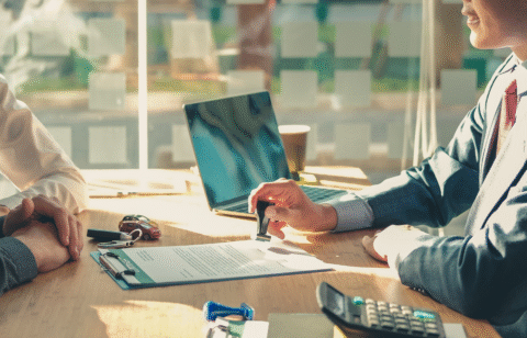 Person stamping a document at a desk with car keys, a calculator, and a laptop nearby.
