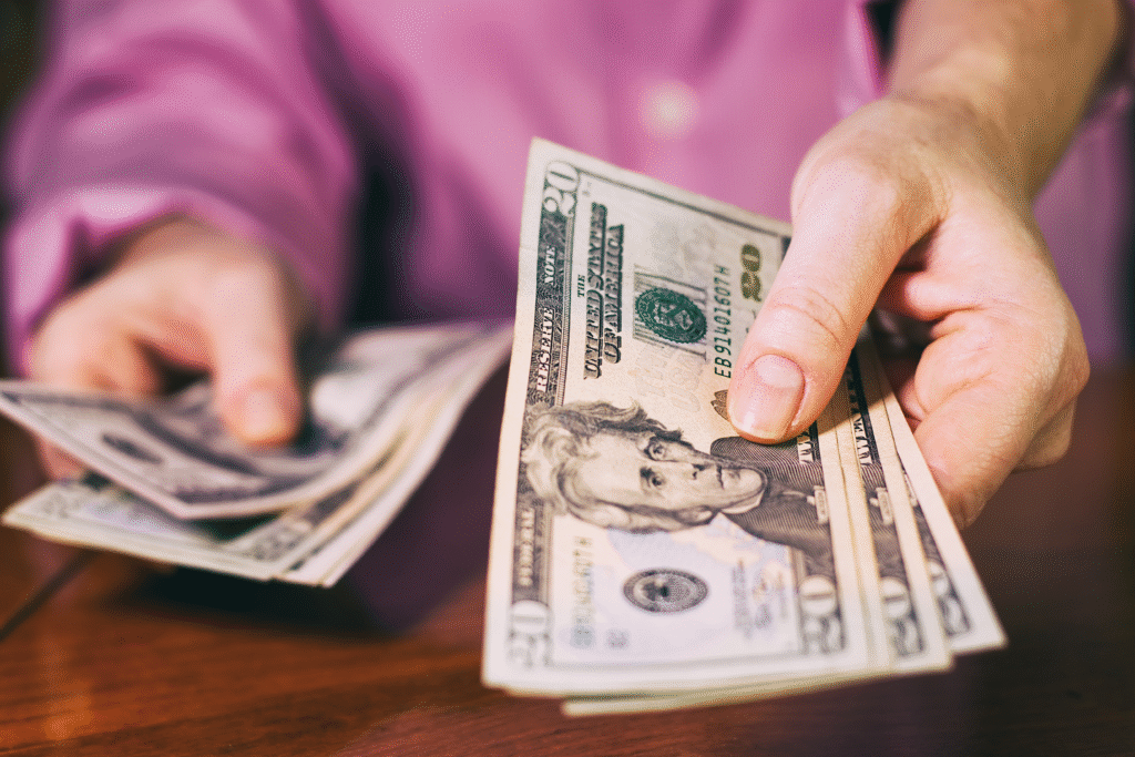 Close-up of a person holding and counting twenty-dollar bills at a table.