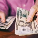 Close-up of a person holding and counting twenty-dollar bills at a table.