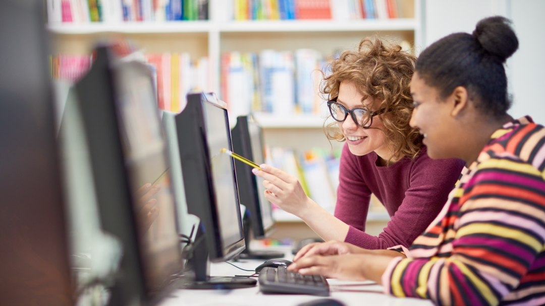 Two college students working together at a computer in a library or computer lab