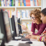Two college students working together at a computer in a library or computer lab
