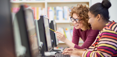 Two college students working together at a computer in a library or computer lab