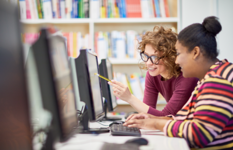 Two college students working together at a computer in a library or computer lab