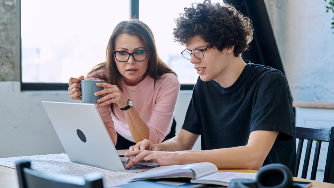 Parent and student reviewing information together on a laptop at a table with books and notes