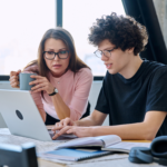 Parent and student reviewing information together on a laptop at a table with books and notes
