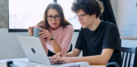 Parent and student reviewing information together on a laptop at a table with books and notes