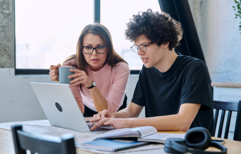 Parent and student reviewing information together on a laptop at a table with books and notes