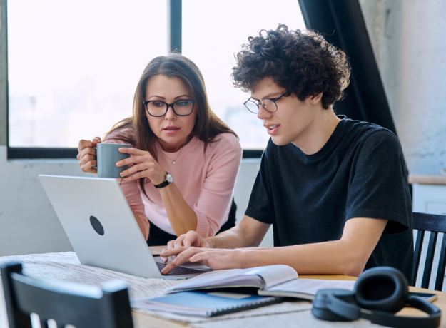 Parent and student reviewing information together on a laptop at a table with books and notes