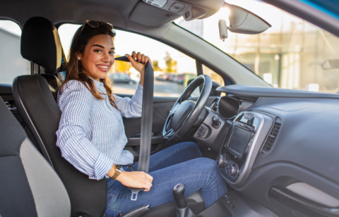 Woman sitting in the driver’s seat fastening her seatbelt inside a car