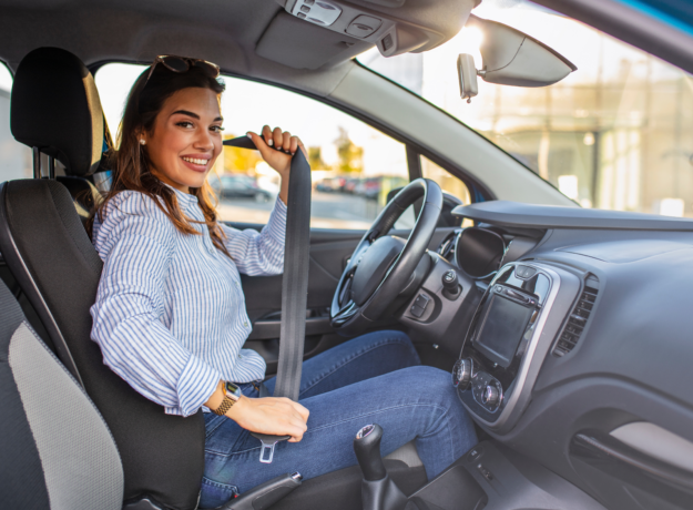 Woman sitting in the driver’s seat fastening her seatbelt inside a car