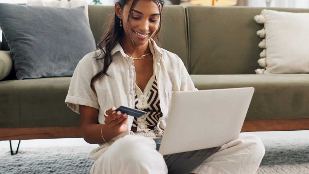 Person sitting on the floor using a laptop while holding a credit card at home.