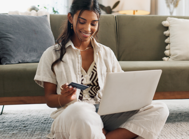 Person sitting on the floor using a laptop while holding a credit card at home.