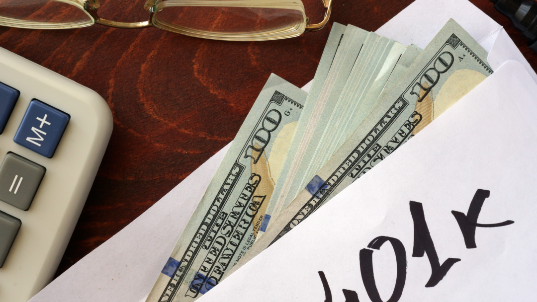 Envelope labeled “401k” with cash partially visible, next to a calculator and eyeglasses on a desk.