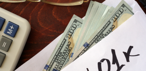 Envelope labeled “401k” with cash partially visible, next to a calculator and eyeglasses on a desk.