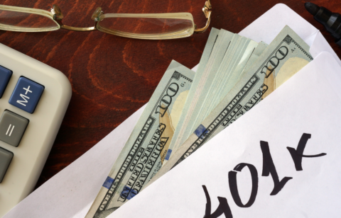 Envelope labeled “401k” with cash partially visible, next to a calculator and eyeglasses on a desk.