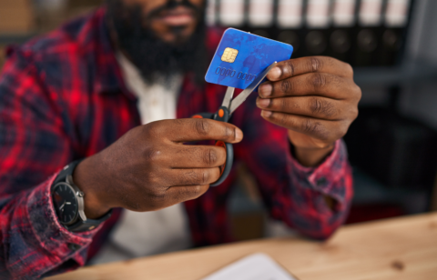 Person using scissors to cut a credit card while sitting at a desk.