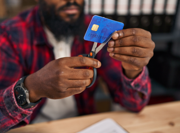 Person using scissors to cut a credit card while sitting at a desk.