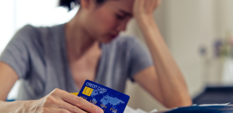 Person holding a credit card while reviewing bills at a table, with their hand on their forehead in a worried pose.