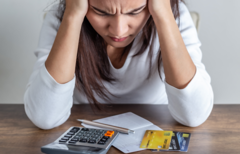 Person holding their head while looking down at a calculator, receipt, and credit cards on a table.