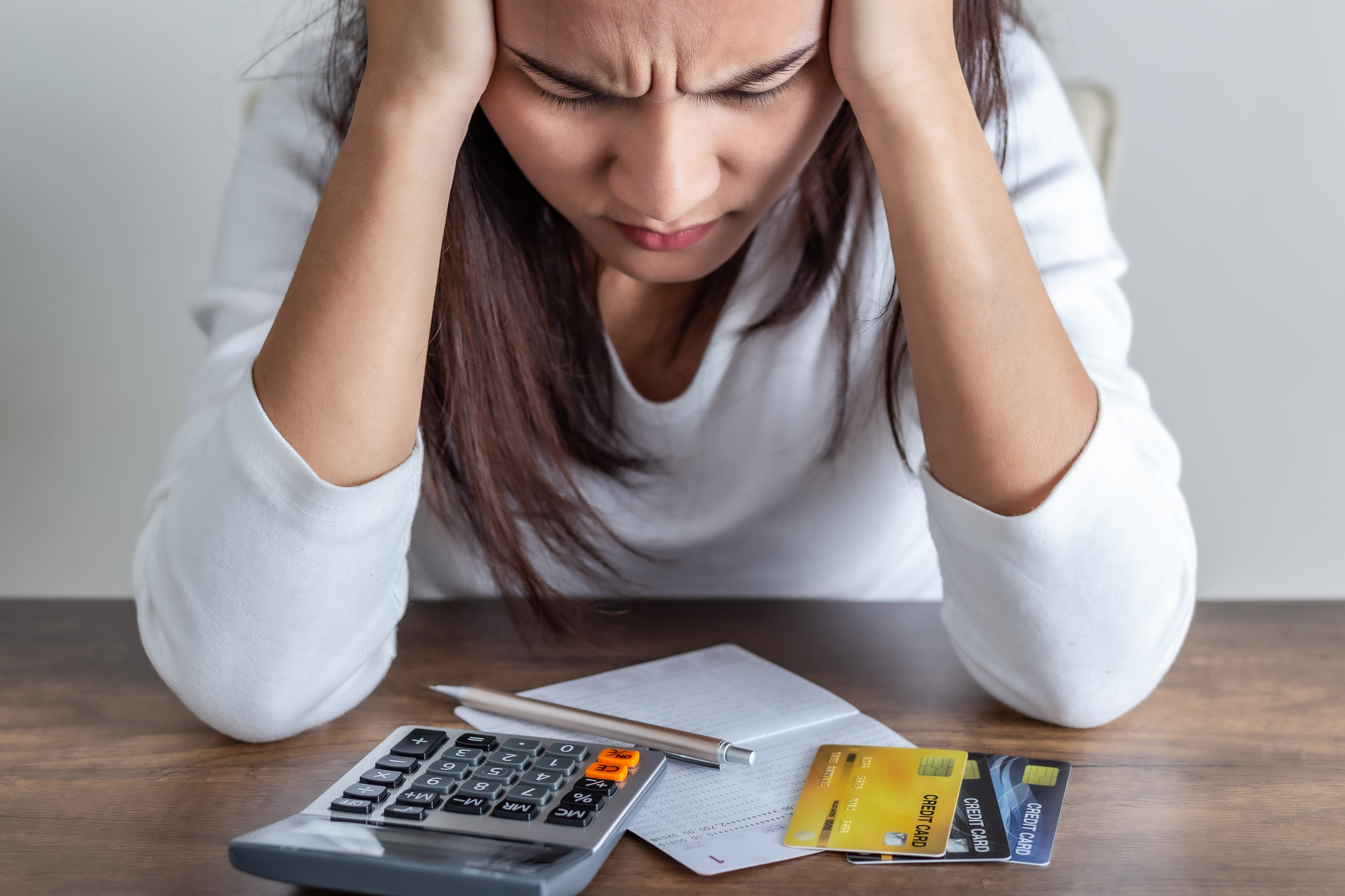 Person holding their head while looking down at a calculator, receipt, and credit cards on a table.