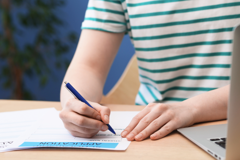 Person filling out a loan application form with a pen next to a laptop
