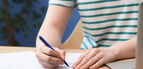 Person filling out a loan application form with a pen next to a laptop
