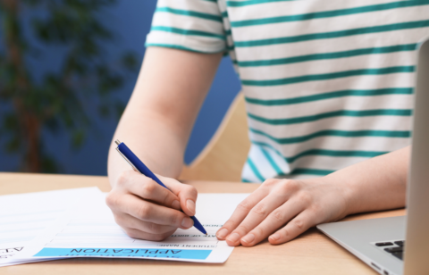 Person filling out a loan application form with a pen next to a laptop