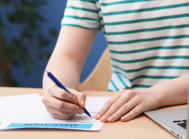 Person filling out a loan application form with a pen next to a laptop