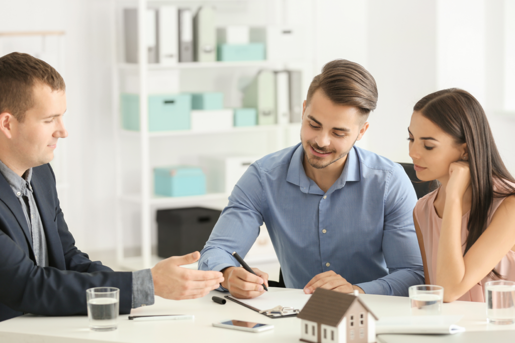 Couple signing paperwork with a professional at a desk, with a small house model in front