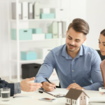 Couple signing paperwork with a professional at a desk, with a small house model in front