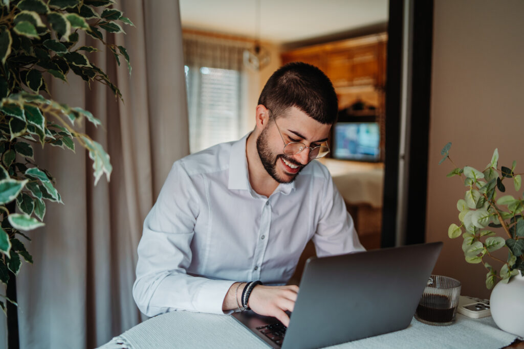 Young man happily working from home using laptop