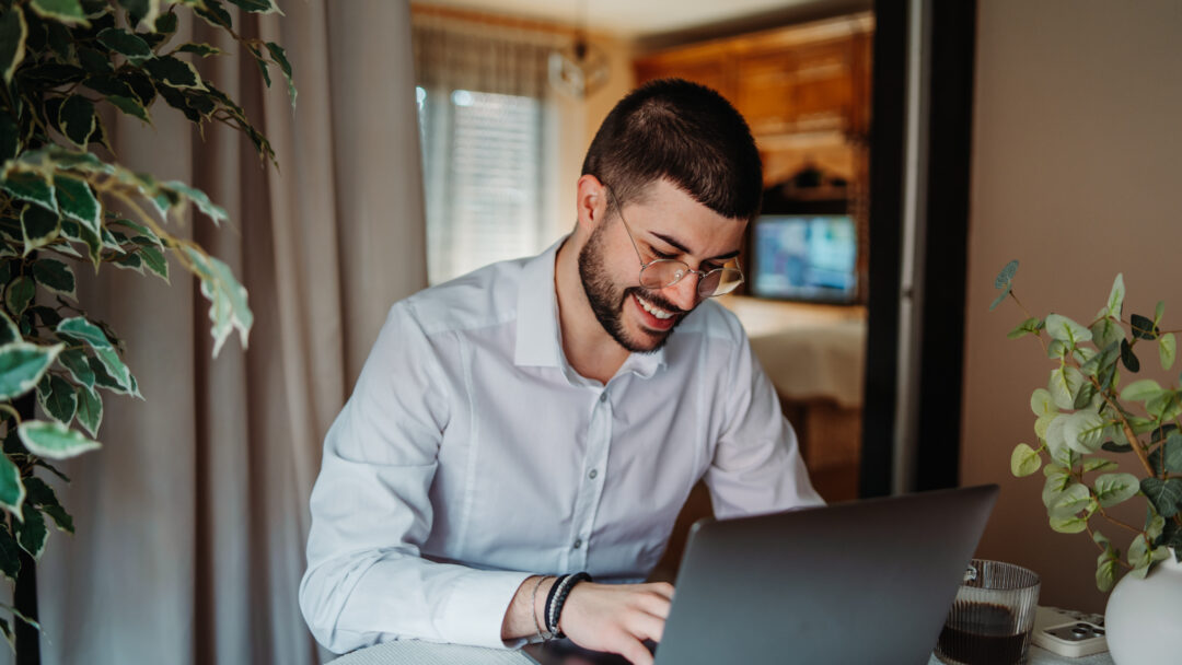 Young man happily working from home using laptop