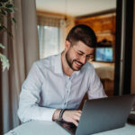 Young man happily working from home using laptop