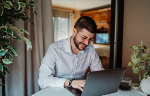 Young man happily working from home using laptop