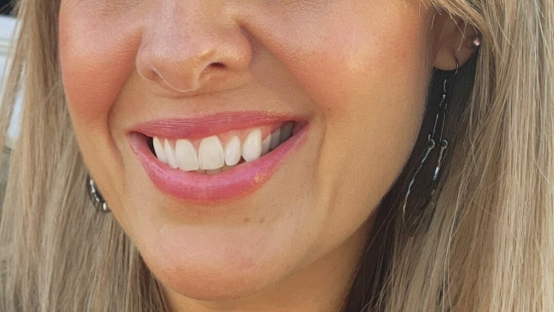 Close-up portrait of a smiling woman with long blonde hair outdoors.