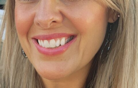 Close-up portrait of a smiling woman with long blonde hair outdoors.