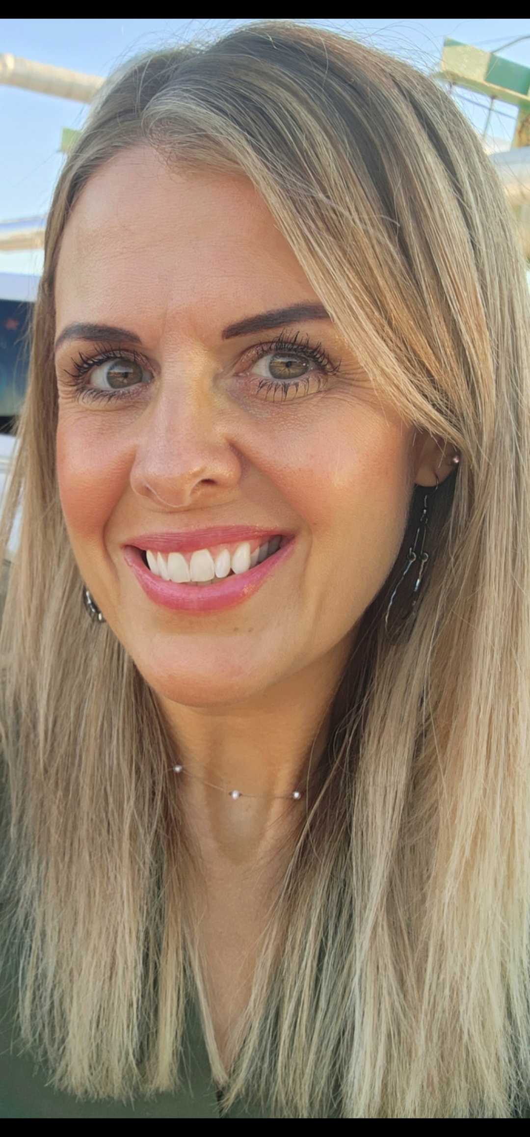 Close-up portrait of a smiling woman with long blonde hair outdoors.