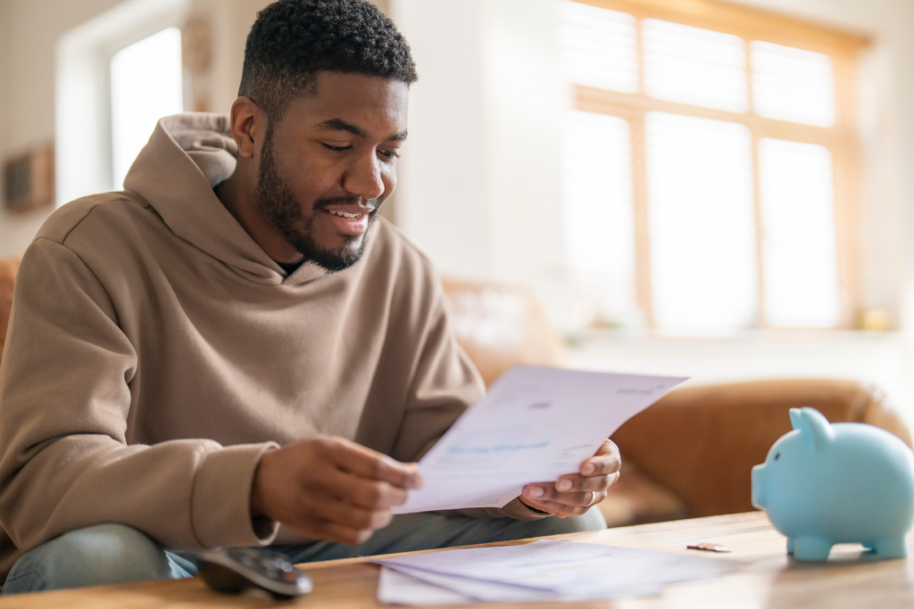 Man sitting at a table reviewing a document with a piggy bank nearby.