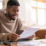 Man sitting at a table reviewing a document with a piggy bank nearby.