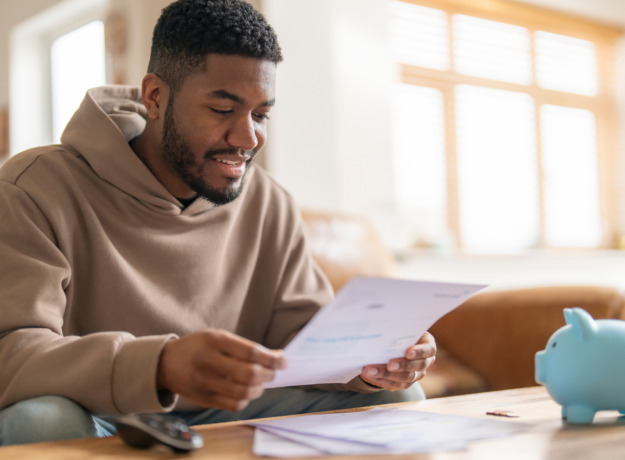 Man sitting at a table reviewing a document with a piggy bank nearby.