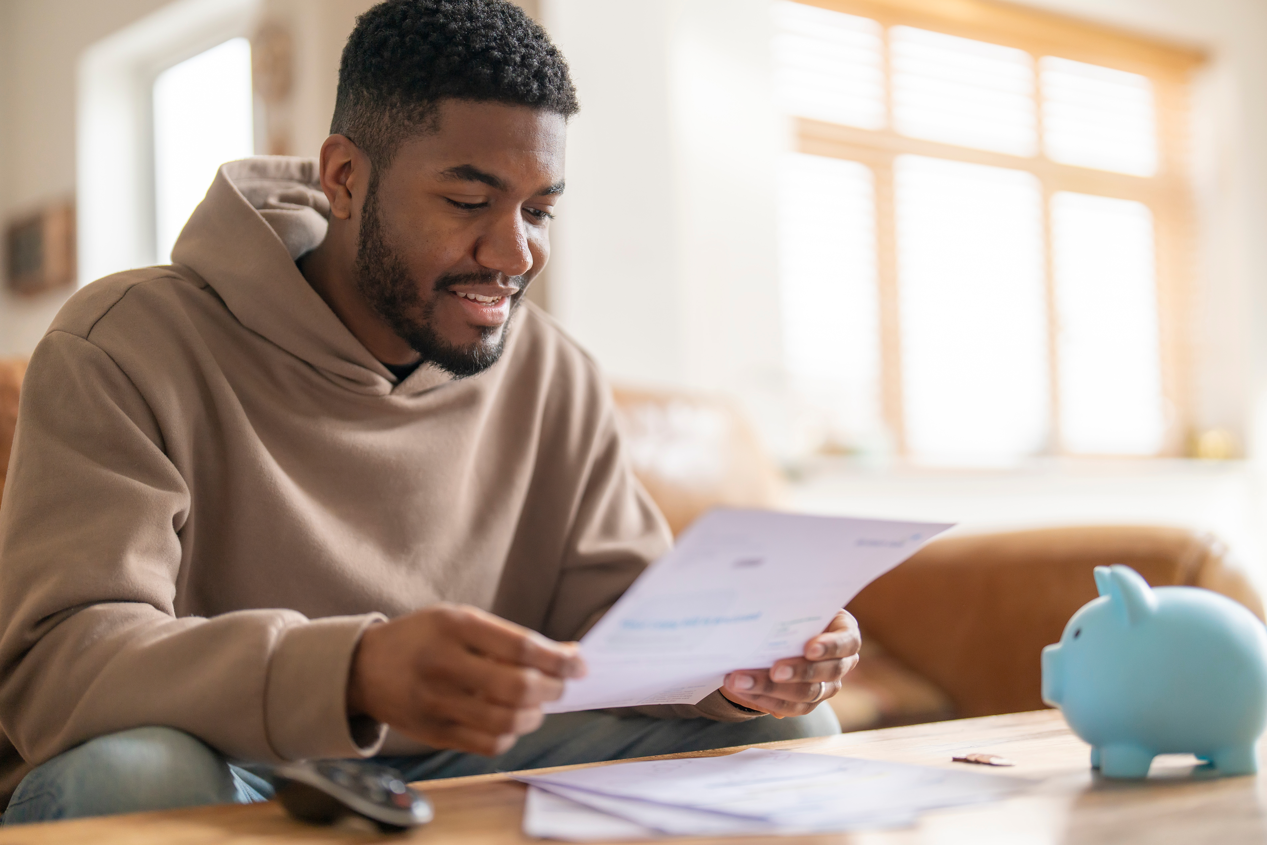 Man sitting at a table reviewing a document with a piggy bank nearby.