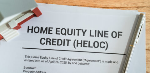 Document titled “Home Equity Line of Credit (HELOC)” on a desk with a pen and small house model nearby.