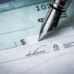 Close-up of a pen writing on a blank check with the dollar amount line visible.