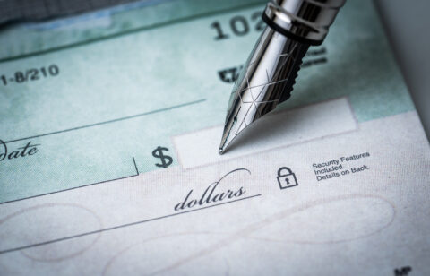 Close-up of a pen writing on a blank check with the dollar amount line visible.