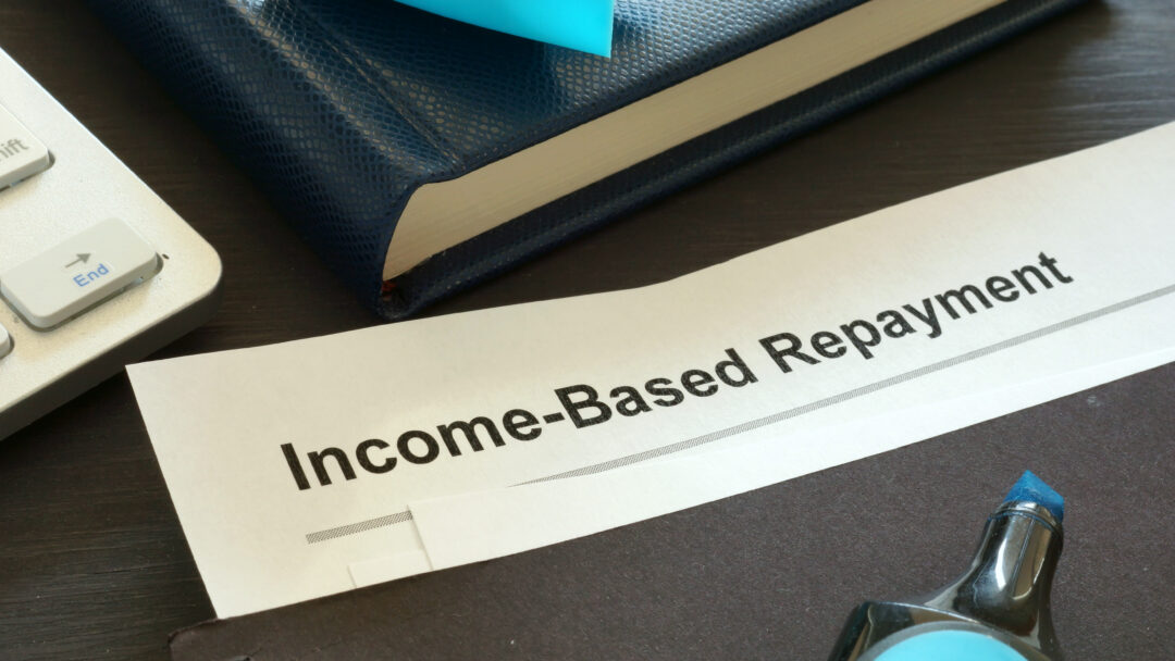Close-up of a document labeled “Income-Based Repayment” on a desk with a notebook, keyboard, and office supplies.
