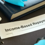 Close-up of a document labeled “Income-Based Repayment” on a desk with a notebook, keyboard, and office supplies.