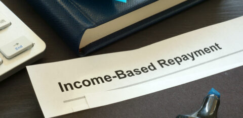 Close-up of a document labeled “Income-Based Repayment” on a desk with a notebook, keyboard, and office supplies.
