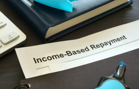 Close-up of a document labeled “Income-Based Repayment” on a desk with a notebook, keyboard, and office supplies.