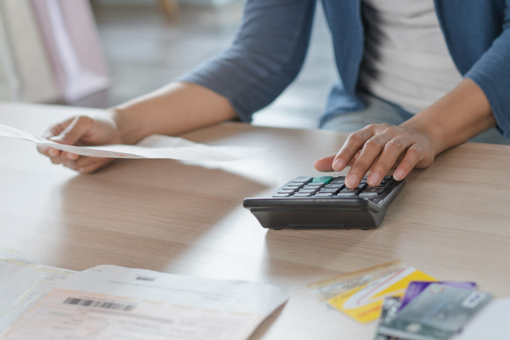 Person using a calculator while reviewing bills and holding a document at a desk.