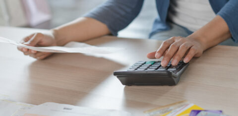 Person using a calculator while reviewing bills and holding a document at a desk.
